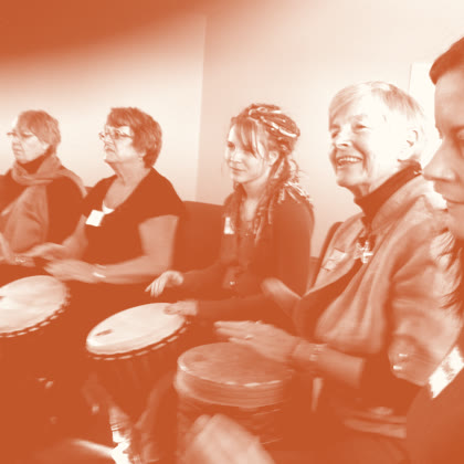 Women of different ages smiling side by side as they drum together