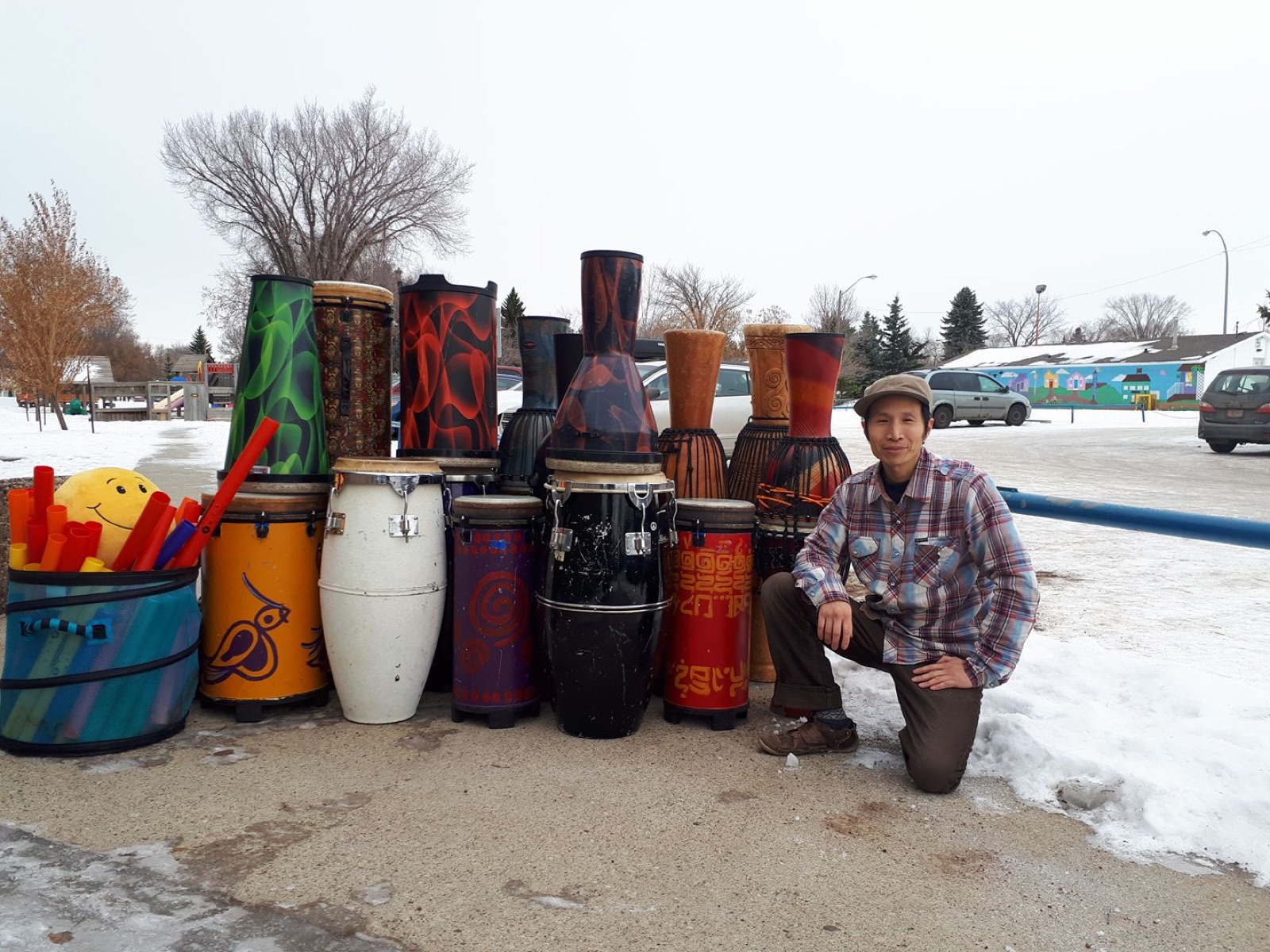 Marcus Fung kneeling beside a collection of hand drums outdoors