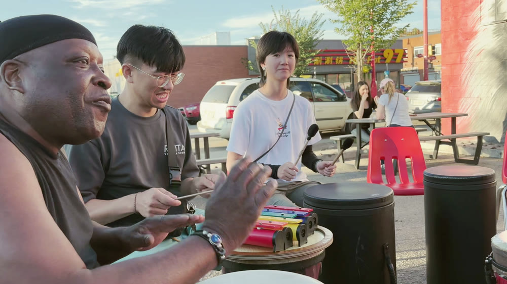 Community members playing drums and a xylophone at an outdoor drum circle